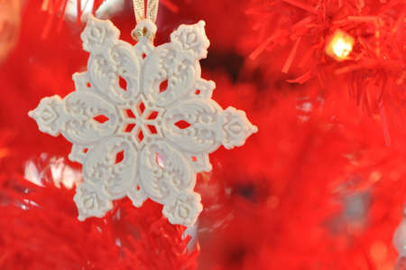 A white snowflake ornament against a red tree backgroundの写真素材