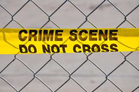 Closeup of Bright yellow Crime Scene Do Not Cross tape against a chain link fenceの写真素材