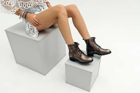 Sensual woman's legs in the boots sitting on a cube over white background. Fashionable bootsの写真素材