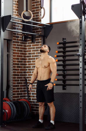 Muscular young shirtless man prepare to doing intense workout on gymnastic rings. Strength or calisthenics workout. Crossfit concept.の写真素材