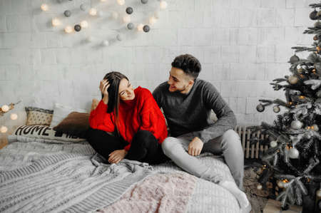 Cheerful couple in winter sweaters having fun lying on cozy bed and laughing , woman hugging her boyfriend spending winter holidays at home in warm and romantic atmosphere.の写真素材