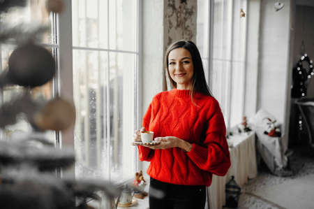 Morning of a happy woman in red sweater enjoying coffee in a winter holiday atmoshpere