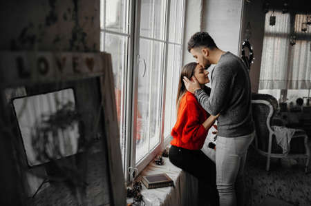 Young man in love kissing his girlfriend on the forehead while standing by the window. Winter holidaysの写真素材