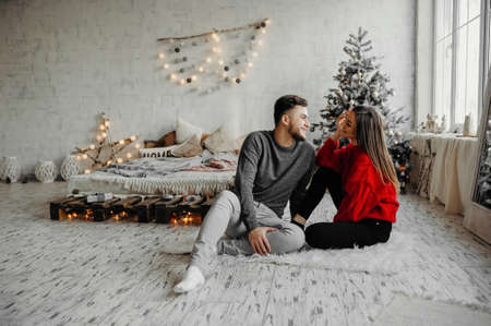 Young couple celebrating Christmas spending time together at home while sitting on the floor. Merry...