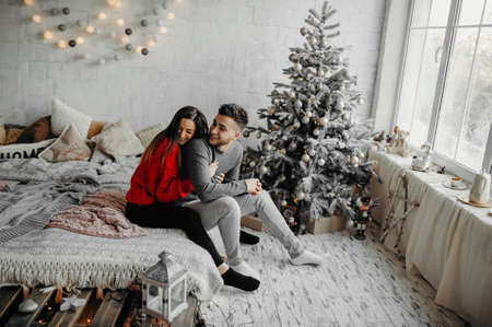 Young happy couple having fun lying on cozy bed and laughing, woman hugging her boyfriend spending winter holidays at home in warm christmas atmosphereの写真素材