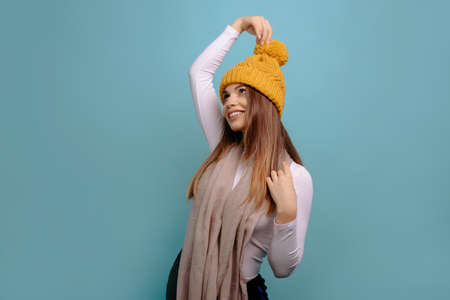 Portrait of playful woman having fun lifting her winter hat up and smiling looking up at the copy space, isolated on a turquoise background.の写真素材
