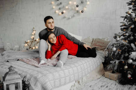 Cheerful couple in winter sweaters having fun lying on cozy bedの写真素材