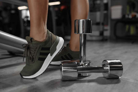 Sport concept. Close up image of a female legs in sneakers with dumbbell next to itの写真素材