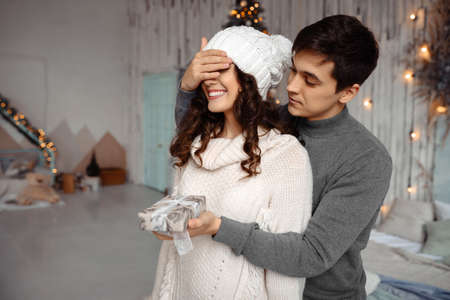 Couple Christmas present. Man keeps his girlfriend eyes covered while he giving a gift, romantic surprise for Christmasの写真素材