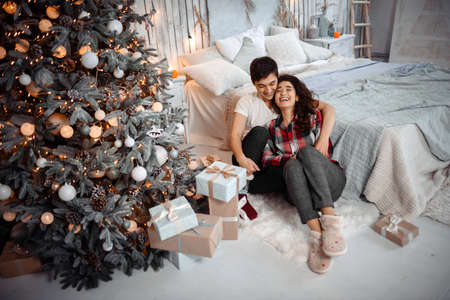Cheerful young woman and man in love have fun with a bunch of presents, enjoying happy moments, celebrating New Years Eve. Happy romantic couple hugging near decorated christmas treeの写真素材