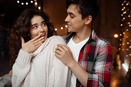 Portrait of a curly amazed woman looking at her boyfriend, have fun together and enjoying New Year holidays moments indoorsの写真素材