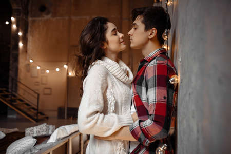 Young beautiful female hugging her boyfriend feeling love spending winter vacation together in cozy interior, romantic couple celebrating New Year dayの写真素材