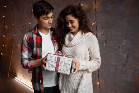 Handsome caucasian man giving christmas present to his loving girlfriend. Lovely young couple celebrating Christmas at homeの写真素材