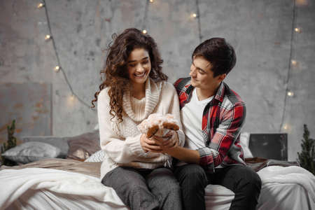 Young couple in love. Man surprising his girlfriend with a yoy hugging her spending winter holidays at home in warm christmas atmosphereの写真素材