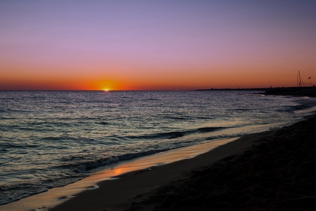 Beautiful Lavender Ocean Sunset with deep orange glow of the setting sun on the horizon over a deserted beach.の写真素材