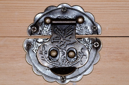 Closeup of an ornate round metal catch lock mounted to a wooden surface.