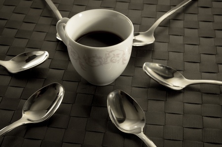 Coffee and teaspoons still life with a freshly brewed cup of aromatic filter coffee surrounded by six silver spoons in a radiating patternの写真素材