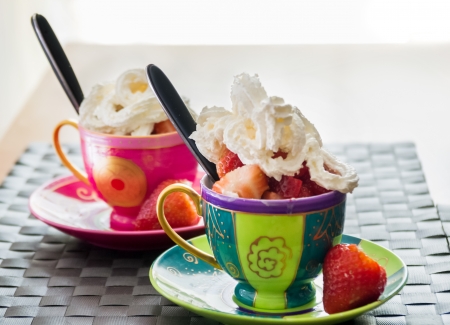 Serving of fresh strawberries and icecream or whipped piped cream in two colourful ceramic cups and saucersの写真素材