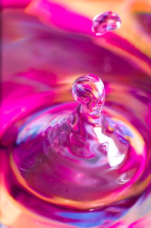 Beautiful vivid pink abstract background of a suspended drop of water or liquid forming a curled column and radiating ripple on the surface of the liquidの写真素材