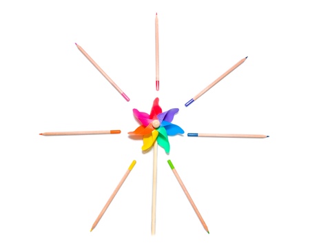 Vivid toy pinwheel in the colours of the spectrum or rainbow encircled by matching radiating coloured pencils in an artistic imaginative arrangement on a white backgroundの写真素材
