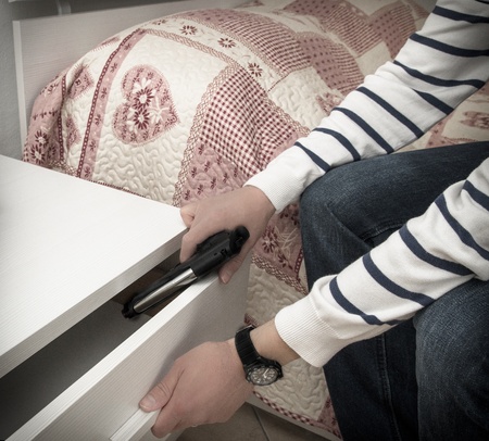Man in a high crime area placing a handgun into the drawer of a bedside table in readiness to defend...