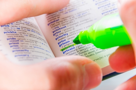 Close-up of a man hands using a florescent green marker to highlight the Privacy word on a dictionaryの写真素材