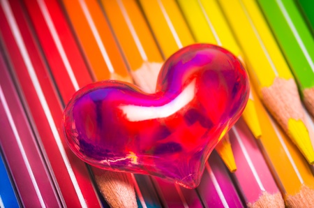 Romantic red translucent heart on a set of vibrant coloured pencils in the colours of the spectrumの写真素材
