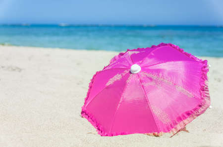 Pretty vibrant pink beach umbrella on the beautiful golden sand of an idyllic tropical beach conceptual of a summer vacation or getawayの写真素材
