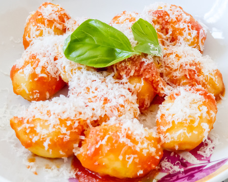Crisp golden Italian semolina pasta and potato dumplings, or gnocci, topped with grated parmesan cheese and fresh basilの写真素材