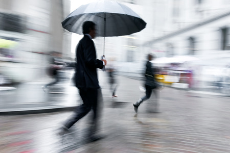 business people walking in the street on a rainy day motion blurredの写真素材
