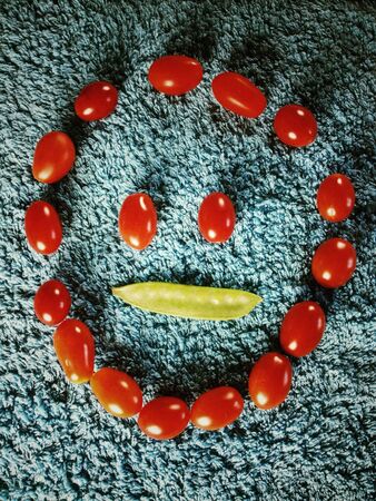 Funny face made with baby plum tomatoes and mange tout on blue の素材