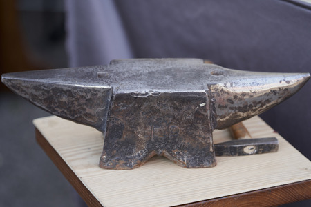 an old anvil and hammer on a wooden tableの写真素材