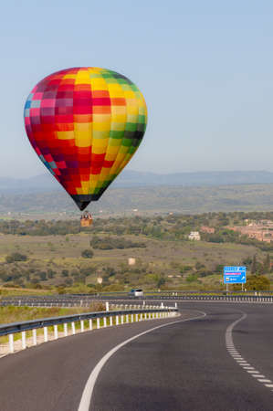 A multicoloured hot air balloon just about landing dangerously on a motorway  Hills and a blue sky in the background の写真素材