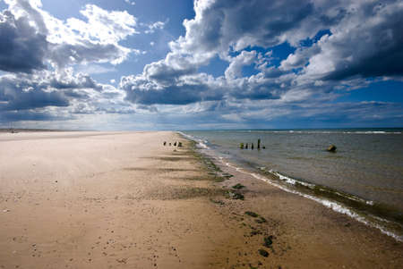 Deserted Norfolk beach at Blakeney, with a calm sea and threatening grey clouds in a blue sky.  Tranquil and lonely scene.の写真素材