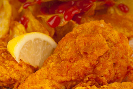 Close up of chicken drumsticks marinated in a chili sauce then deep fried in oatmeal batter, giving a thick, crunchy covering.  Served with potato crisps and tomato sauce, garnished with a lemon sliceの写真素材