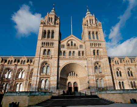 Front  view of the terracotta, romanesque facade of the London Natural History Museum illuminated by  winter sunshine. It was opened in 1881.  The decoration of the columns in the main entrance are based on the bark of fossil trees. Blue sky and clouds.のeditorial素材
