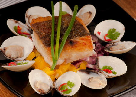 Seared cod fillet with crispy brown skin and accompanied by almejas, clams, yellow pepper and red onion.  garnished with red chili, coriander and chives.  On a black plate.の写真素材