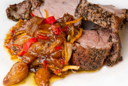 Roast fillet of pork marinaded in dried mint, olive oil and orange zest.  Caramelised garlic and orange skin with orange juice, olive oil and red chili.  On a white plate.の写真素材