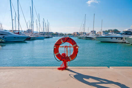 Luxury yachts lined up in Denia marina, Spain.  Orange lifebelt in the foreground.  Sunny with blue sky and light cloud.の写真素材