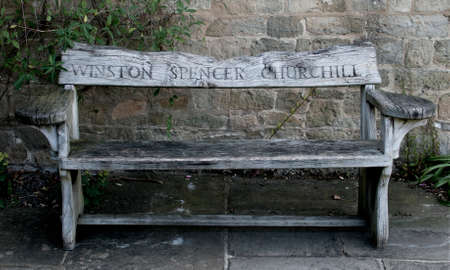 Wooden garden bench with the name Winston Spencer Churchill carved in the back from Chartwell House, Kent, his home until he died in 1965.  Afgainst a stone wall on stone flagging.のeditorial素材