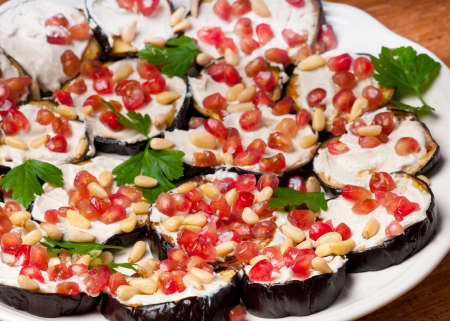 Grilled aubergine slices with tahini yoghurt garnished with pine nuts, pomegranate and parsleyの写真素材