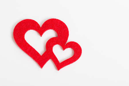 two red hearts of felt come together against white backgroundの写真素材