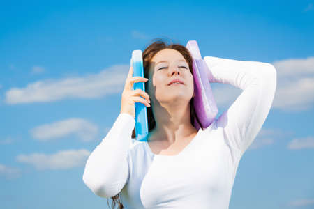 woman against blue sky holding some icepack against her headの写真素材