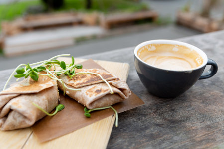 Cup of coffee and wraps with microgreens on wooden table