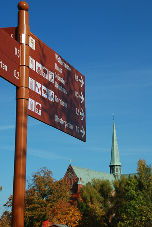 Trail sign in Bad Doberan (Germany) in the background the minster, autumn trees with yellow leaves in the park of the churchの写真素材