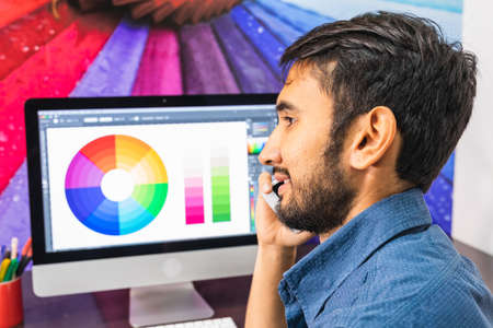 Side view. Young bearded businessman in denim shirt is sitting in office at table. Using his smartphone.の写真素材