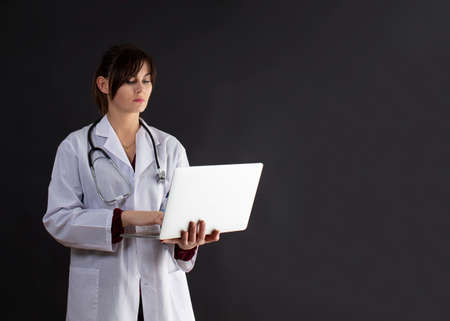 Portrait of confident, beautiful, young medical female doctor on background. The doctor is holding a laptop in her handsの写真素材