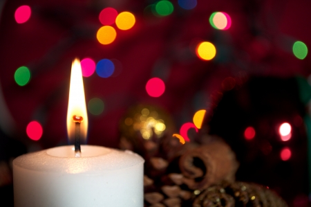 A burning white Christmas Candle with decorations and colorful christmas lights in the background  の写真素材