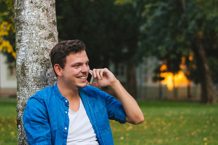 A man is talking on the phone and smiling in parkの写真素材