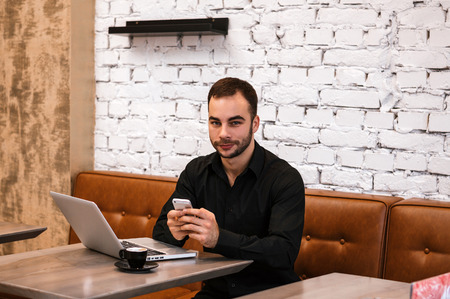 Portrait of businessman with a mobile phone sitting at cafe using laptop